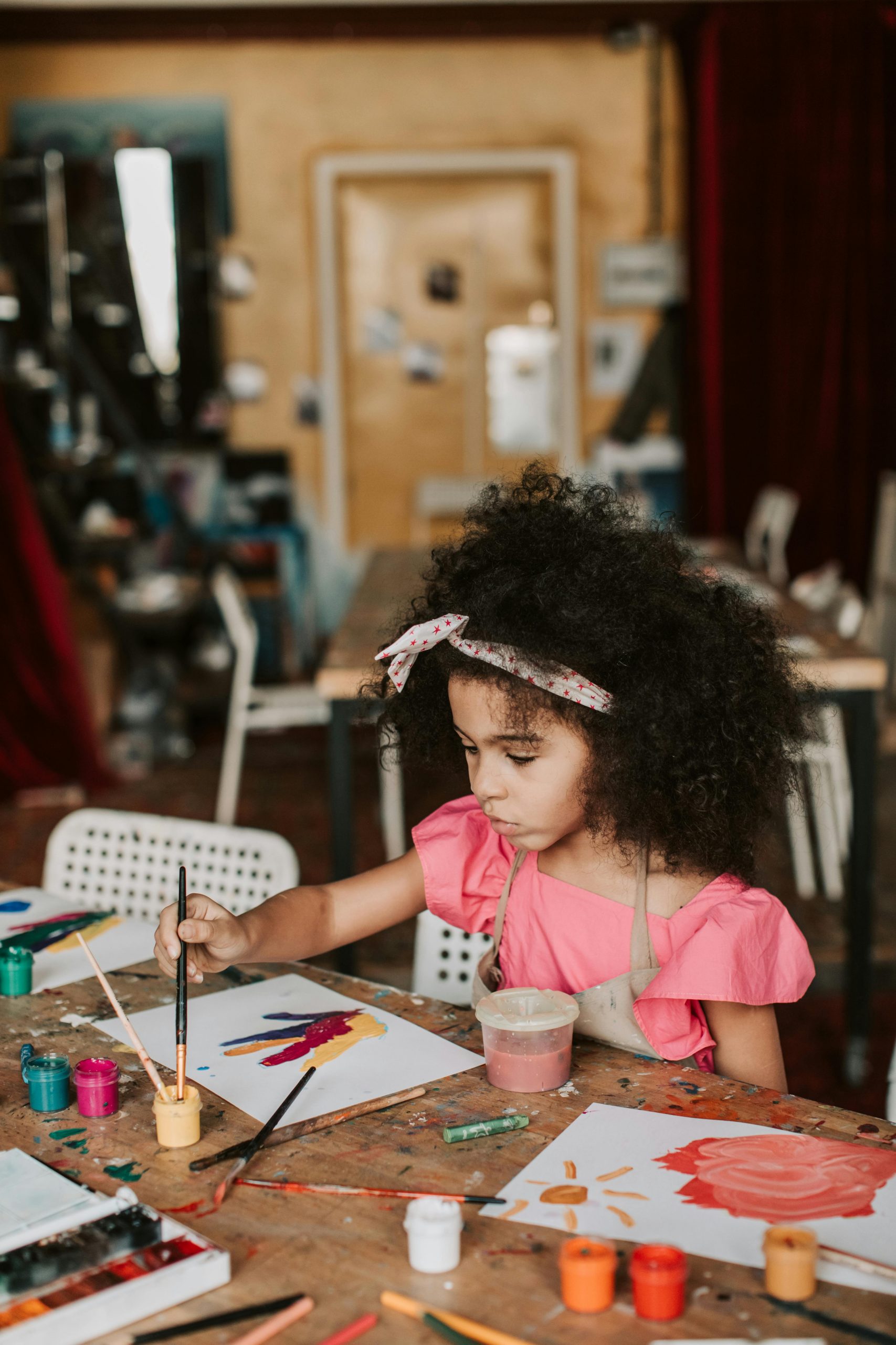 A young girl focuses on her painting in a lively art workshop setting, expressing creativity.