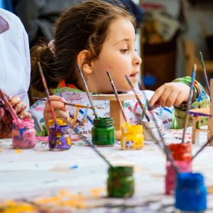 A young girl painting with vibrant colors in an art class, surrounded by paint pots.