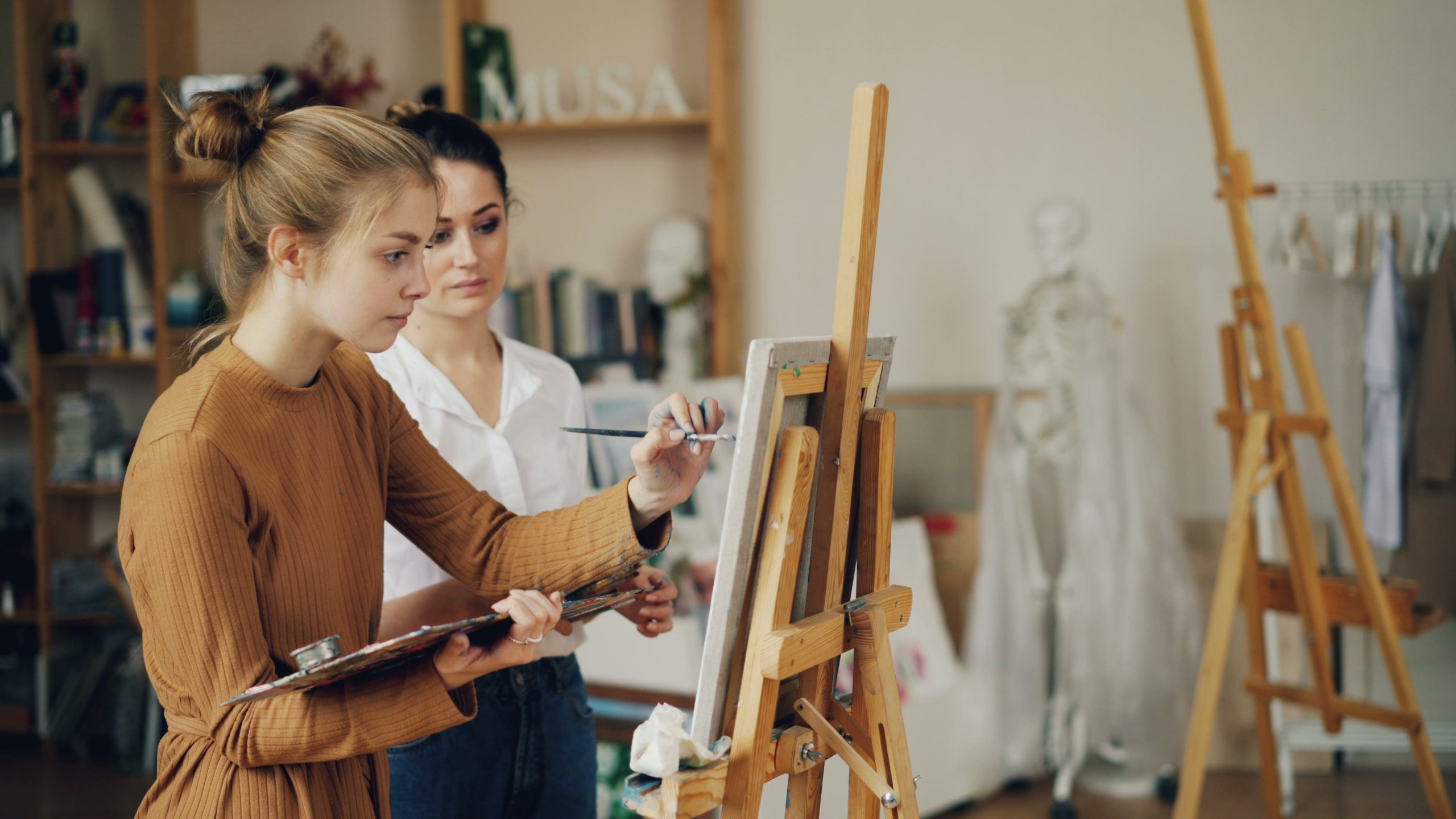 Two women focused on painting at easels in a creative art studio.