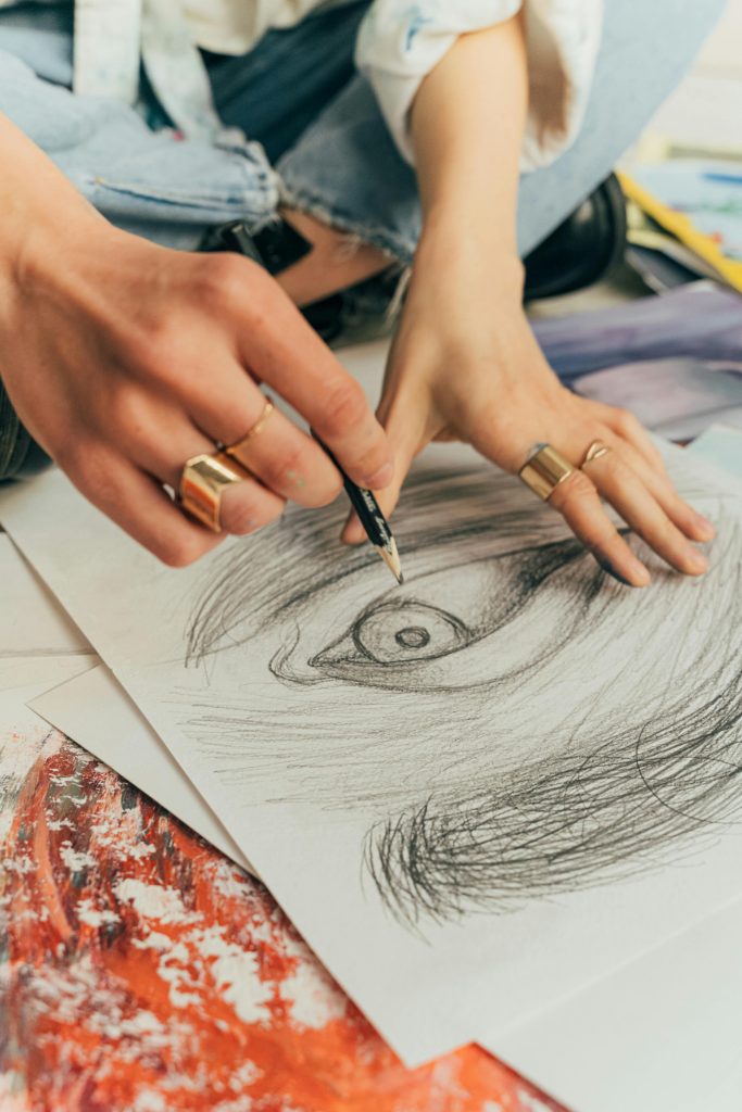 Close-up of hands sketching an eye with pencil on paper, showcasing artistic creativity.